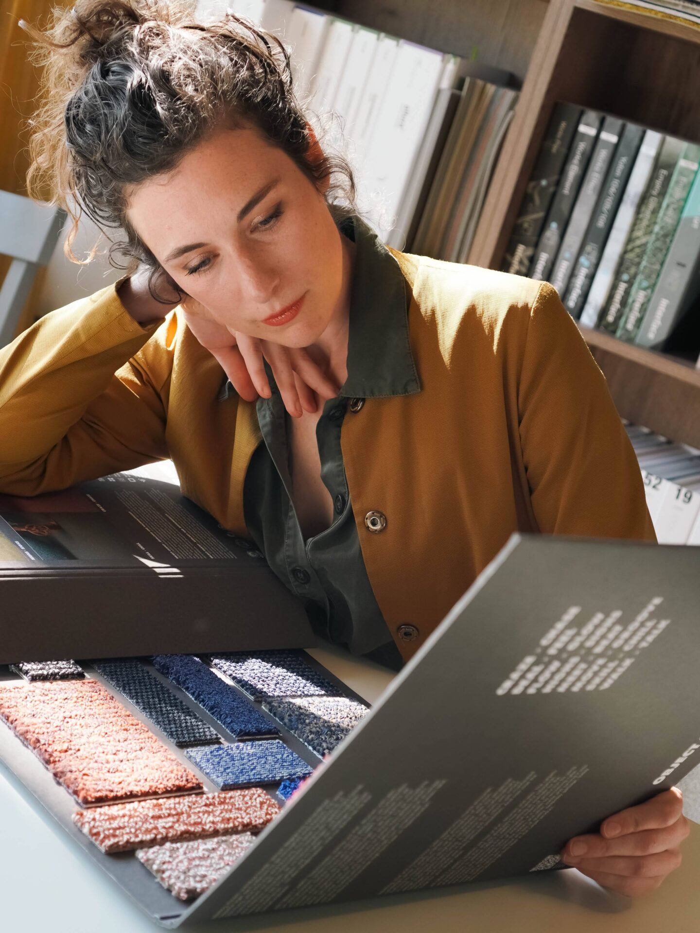 Interieurontwerper bekijkt tapijtstalen in een stalenboek bij het raam